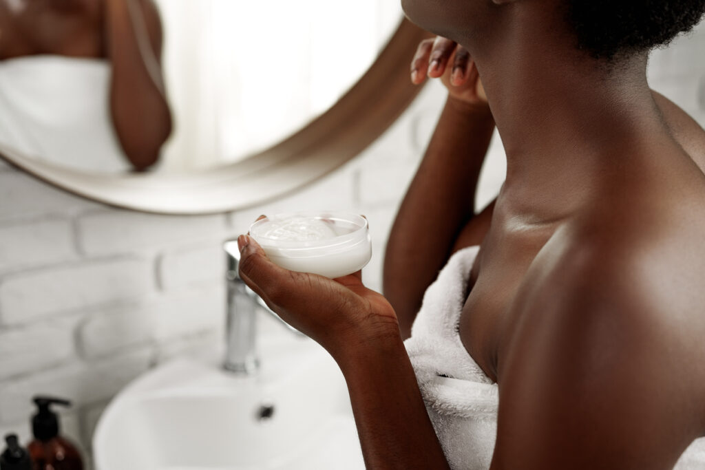 Woman applying moisturizer in a bright bathroom while looking at the mirror in the morning